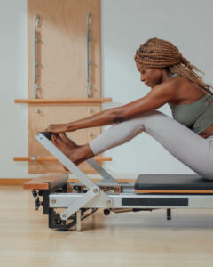 Beautiful African smiling sportswoman doing pilates exercise on reformer. Beautiful African smiling sportswoman doing pilates exercise on reformer.
